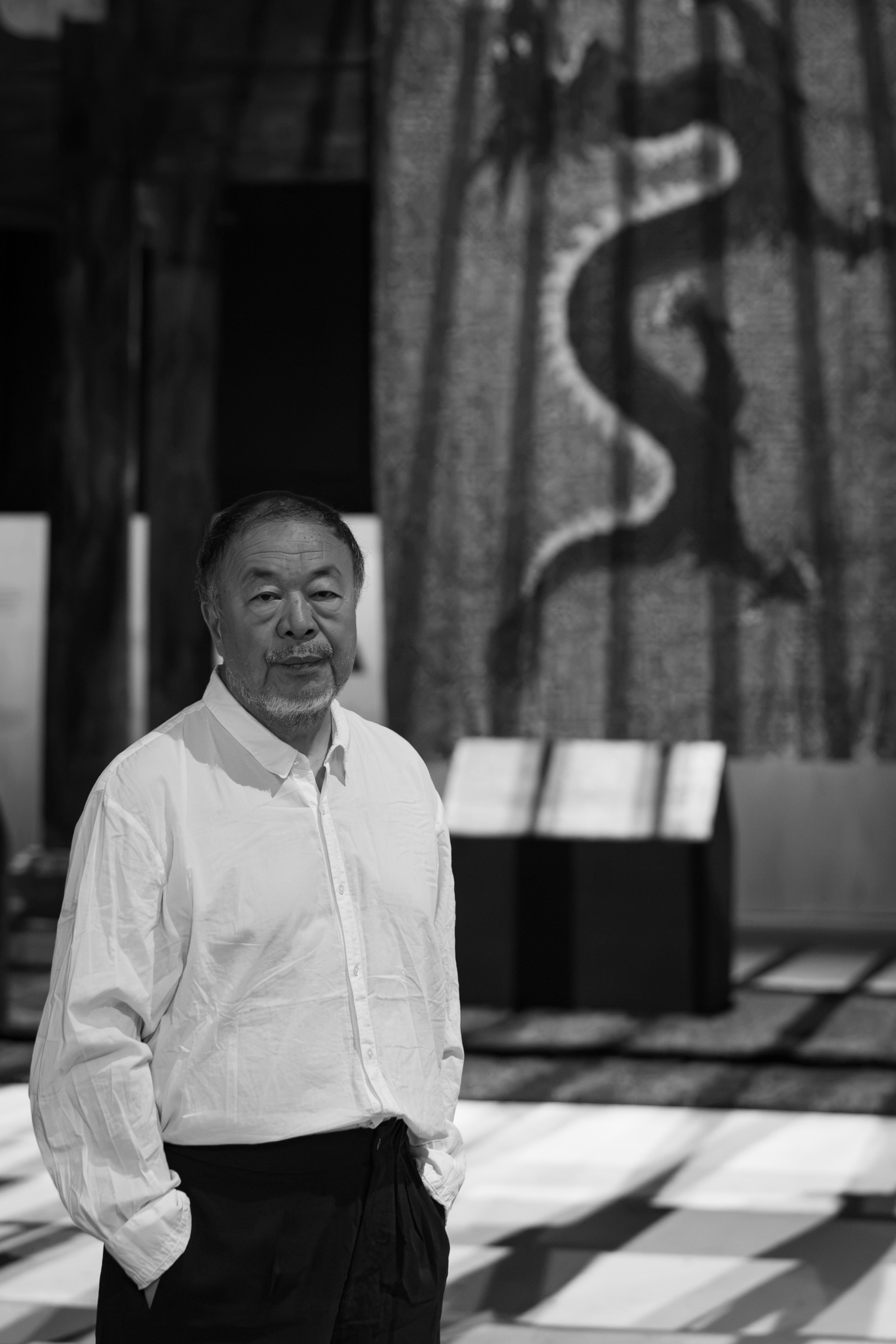 Black-and-white portrait of Ai Weiwei standing inside an installation at Factory International.