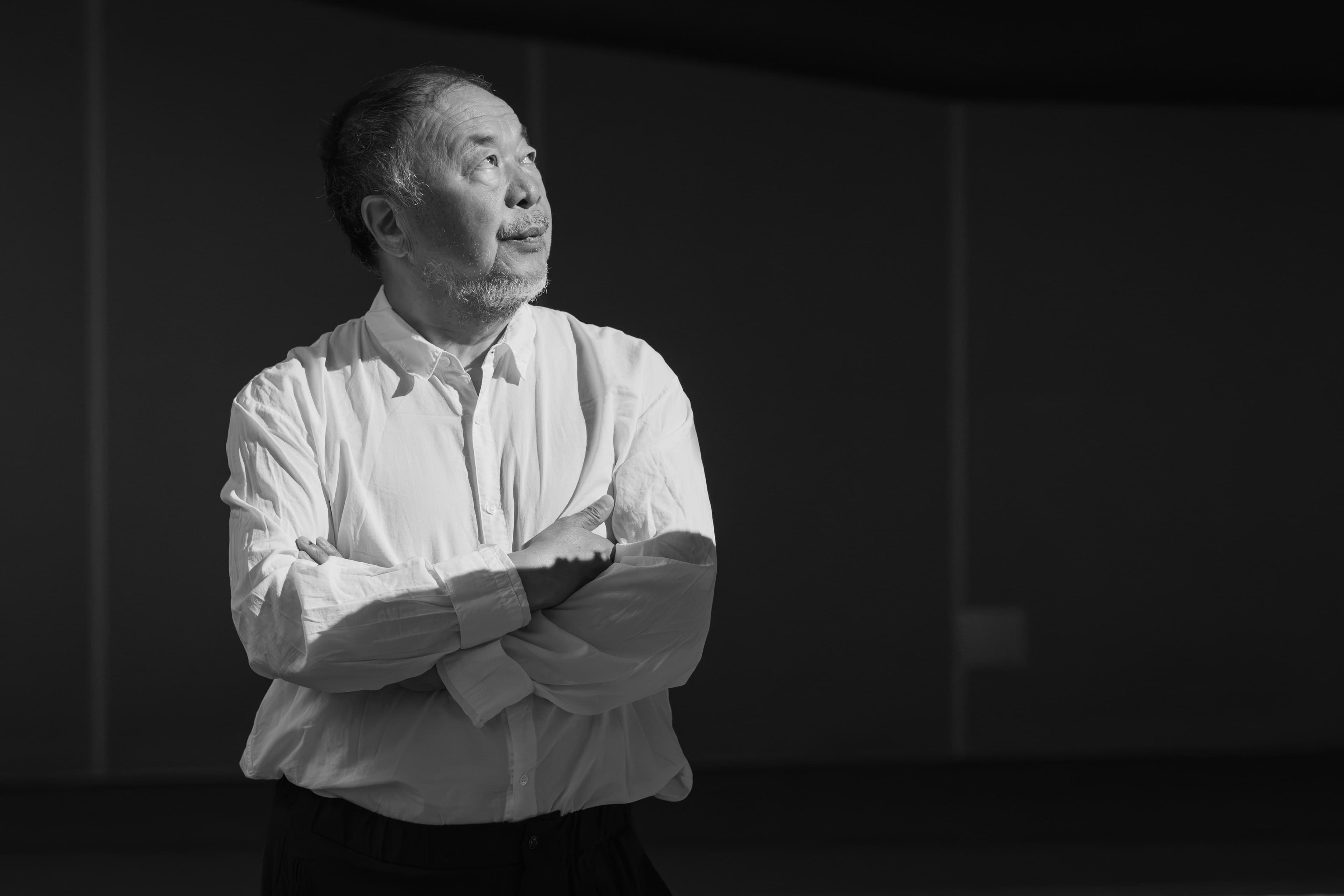 Ai Weiwei seated in front of a large sculptural installation at Factory International.