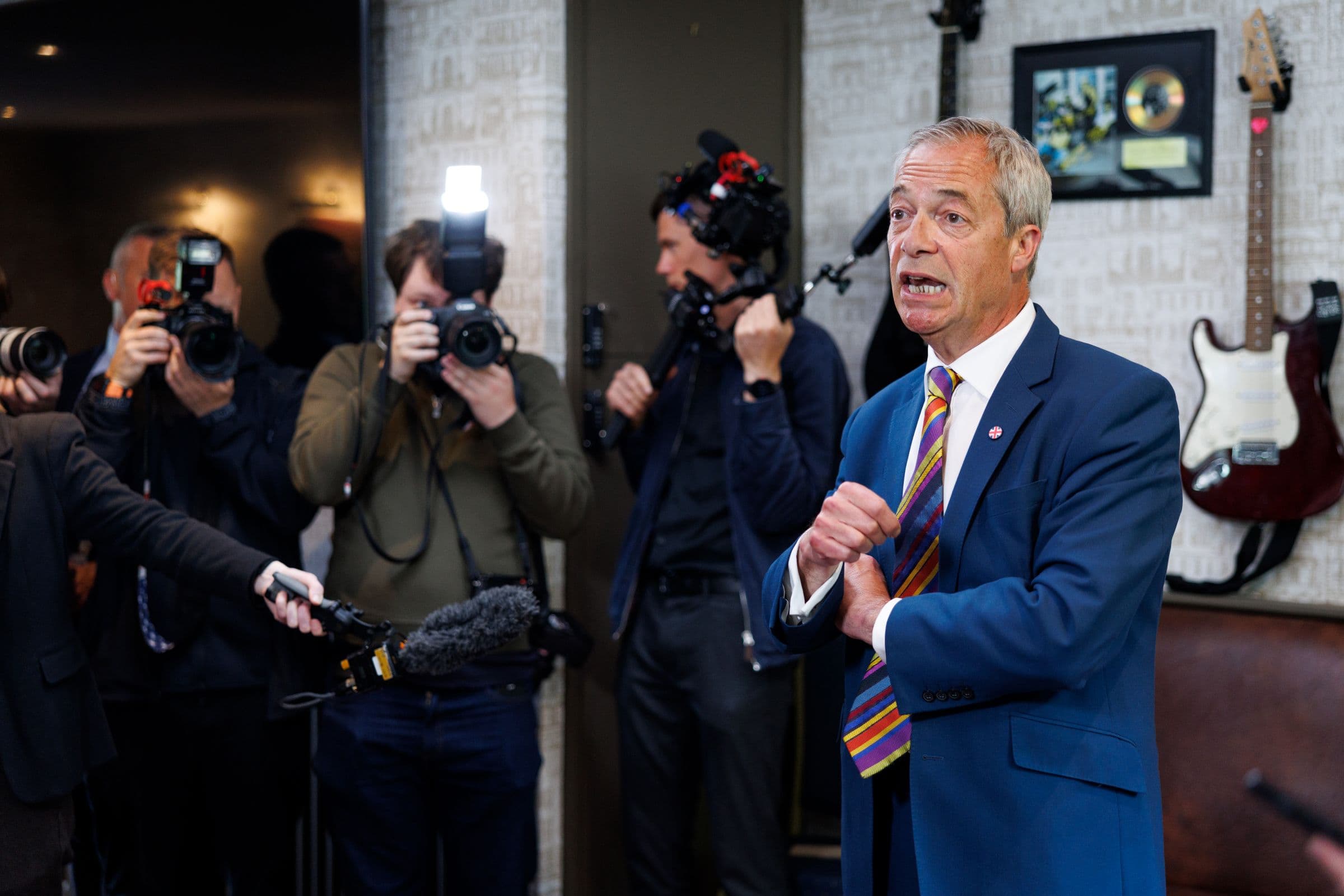 A suited speaker addressing photographers during an editorial media moment.