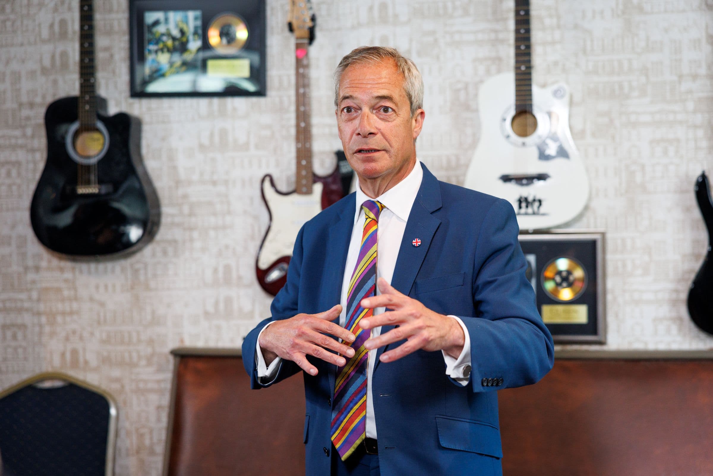 A suited speaker photographed in front of framed guitars and records.