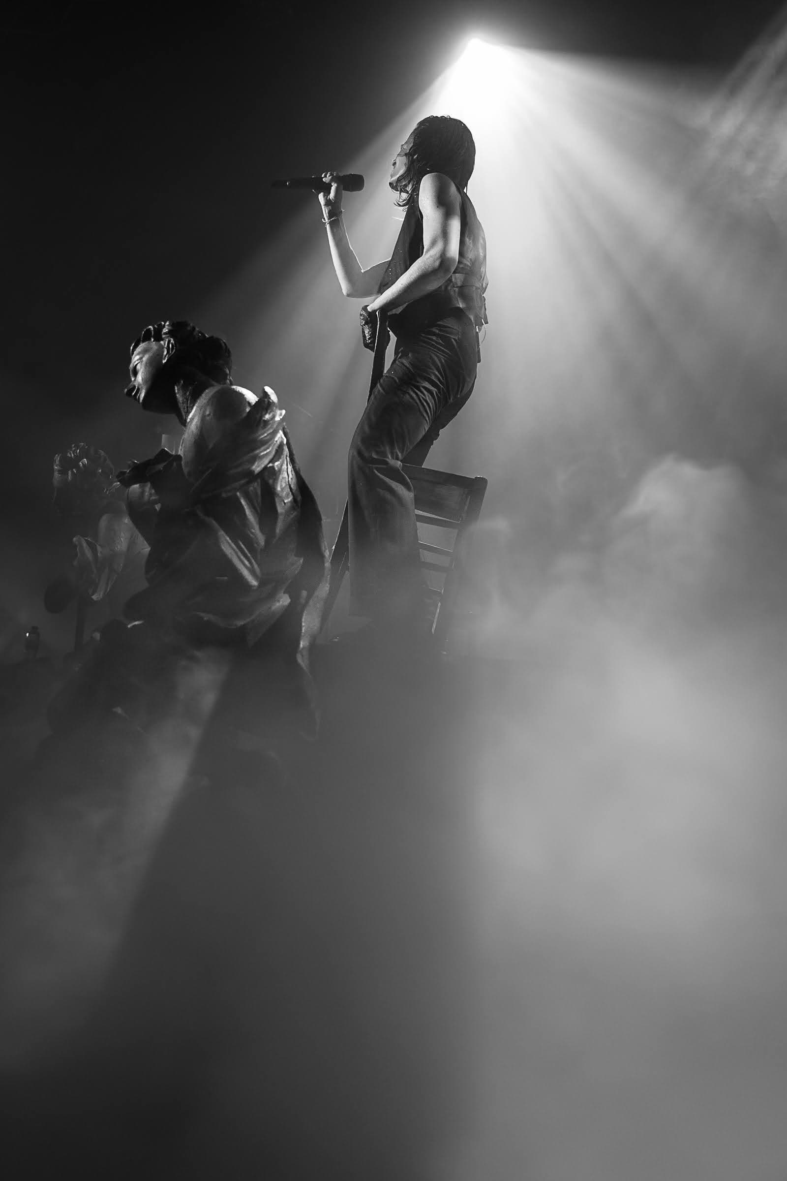 Christine and the Queens performing live in dramatic monochrome stage light.