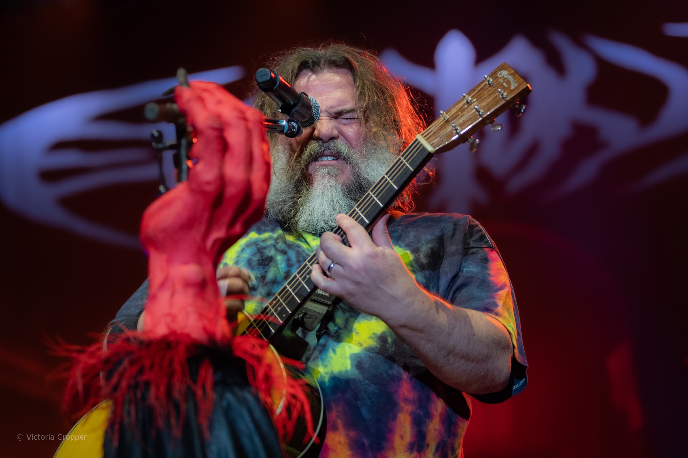 Jack Black performing live at AO Arena in Manchester with a guitarist under colourful stage light.