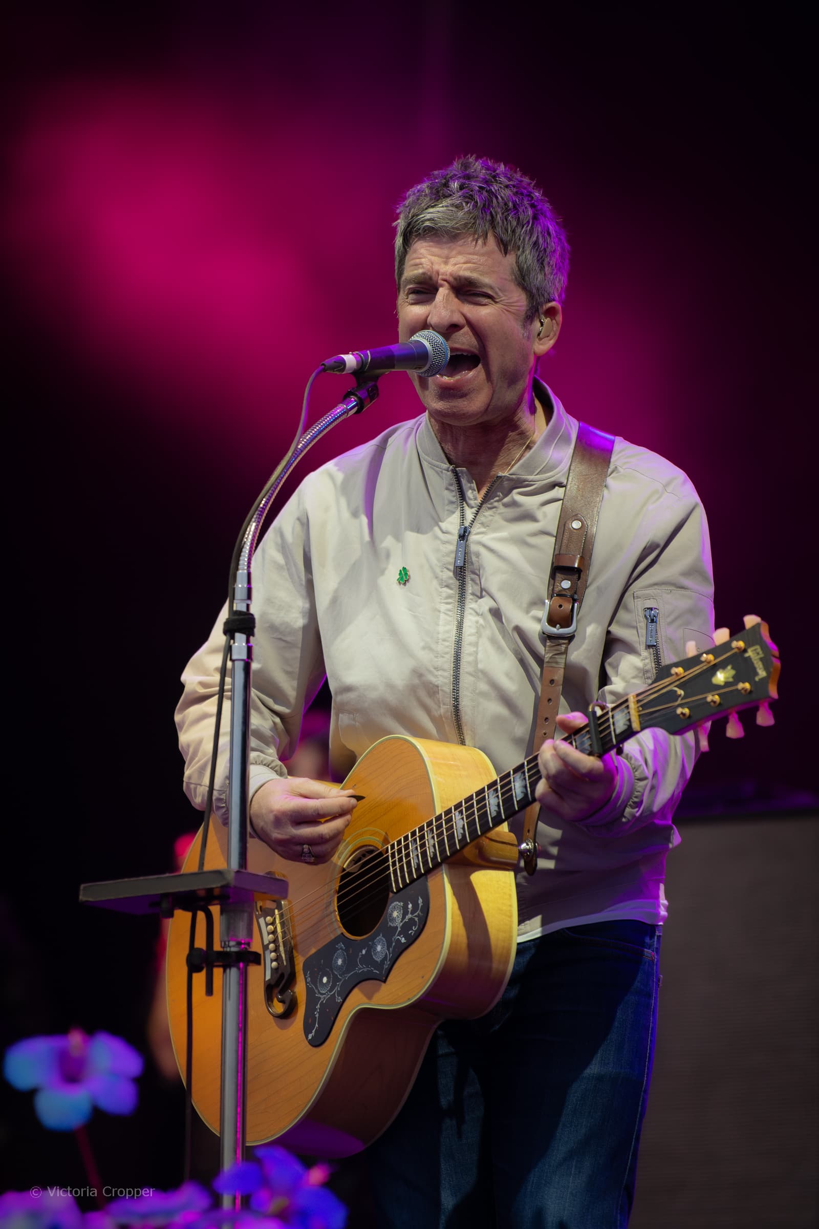 Noel Gallagher performing live with an acoustic guitar.